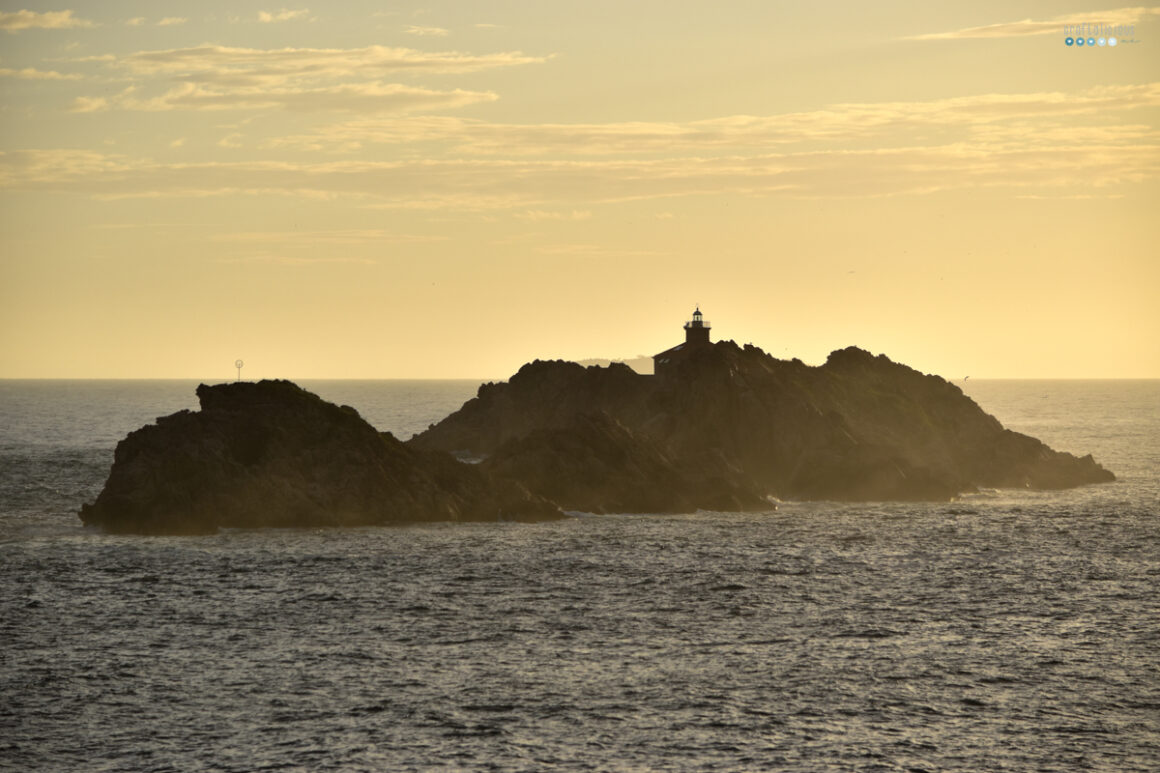 a small rocky island with a lighthouse in a yellow hazy evening light