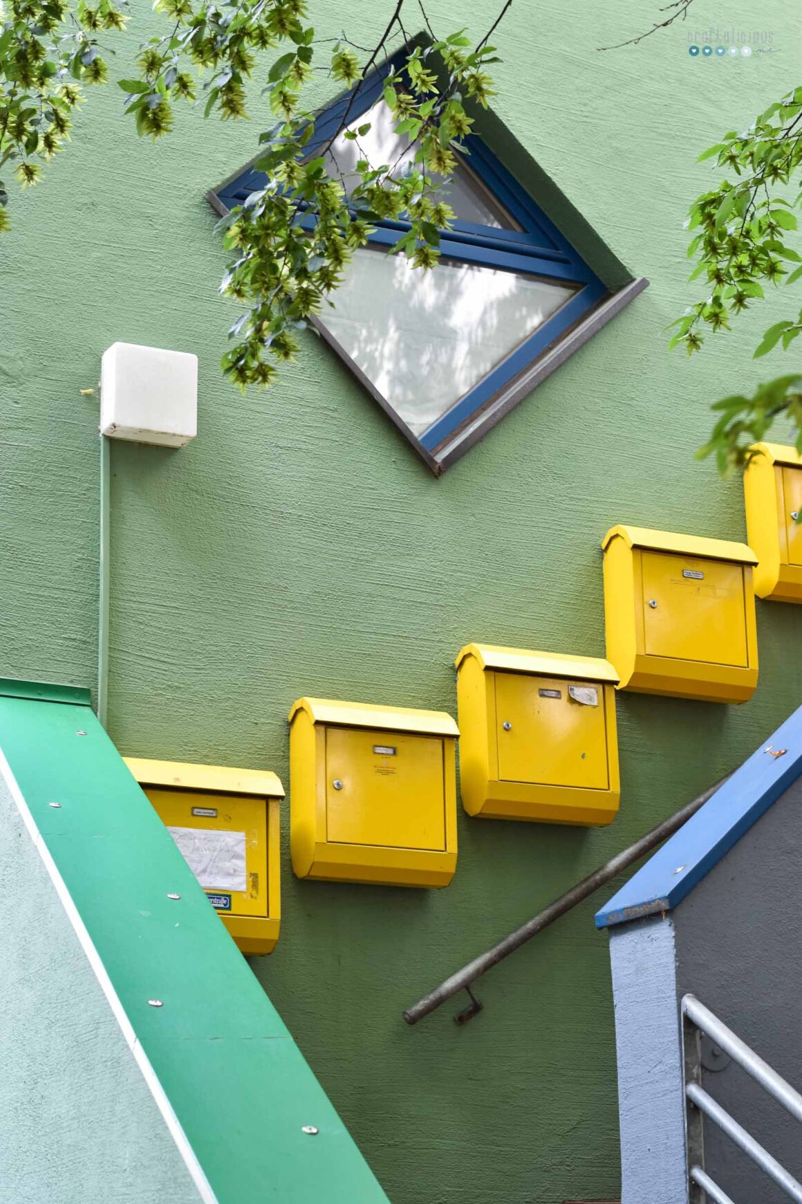 yellow mail boxes on a green wall, diagonally hung along the stair case, above a square window