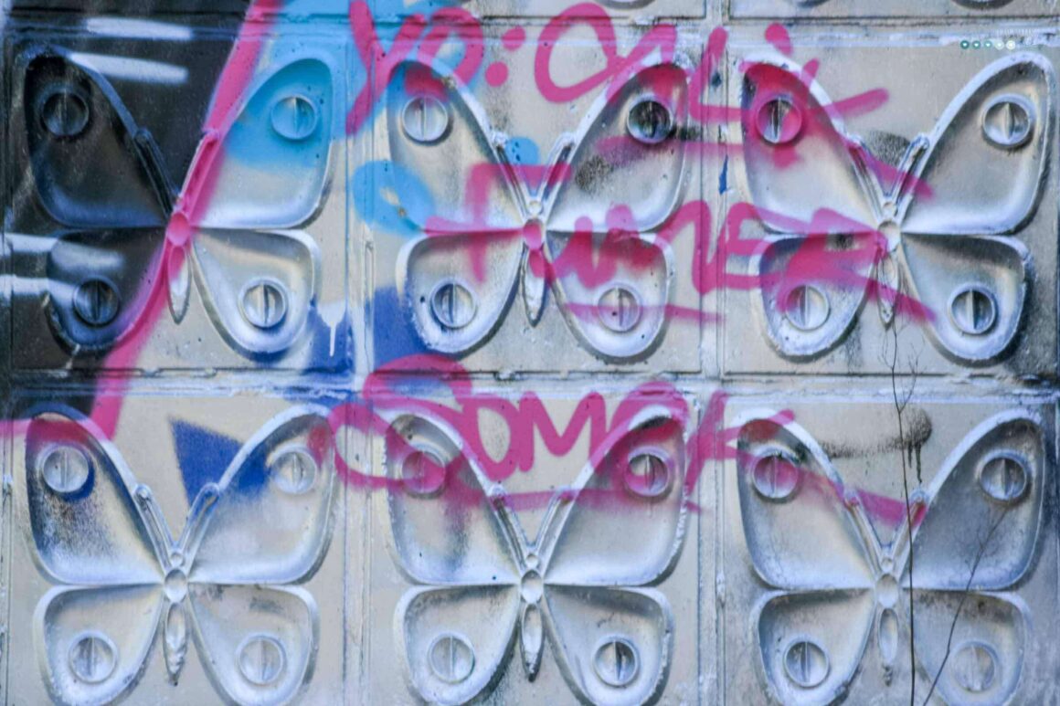 a graffiti covered wall. the wall has relieved butterfly tiles